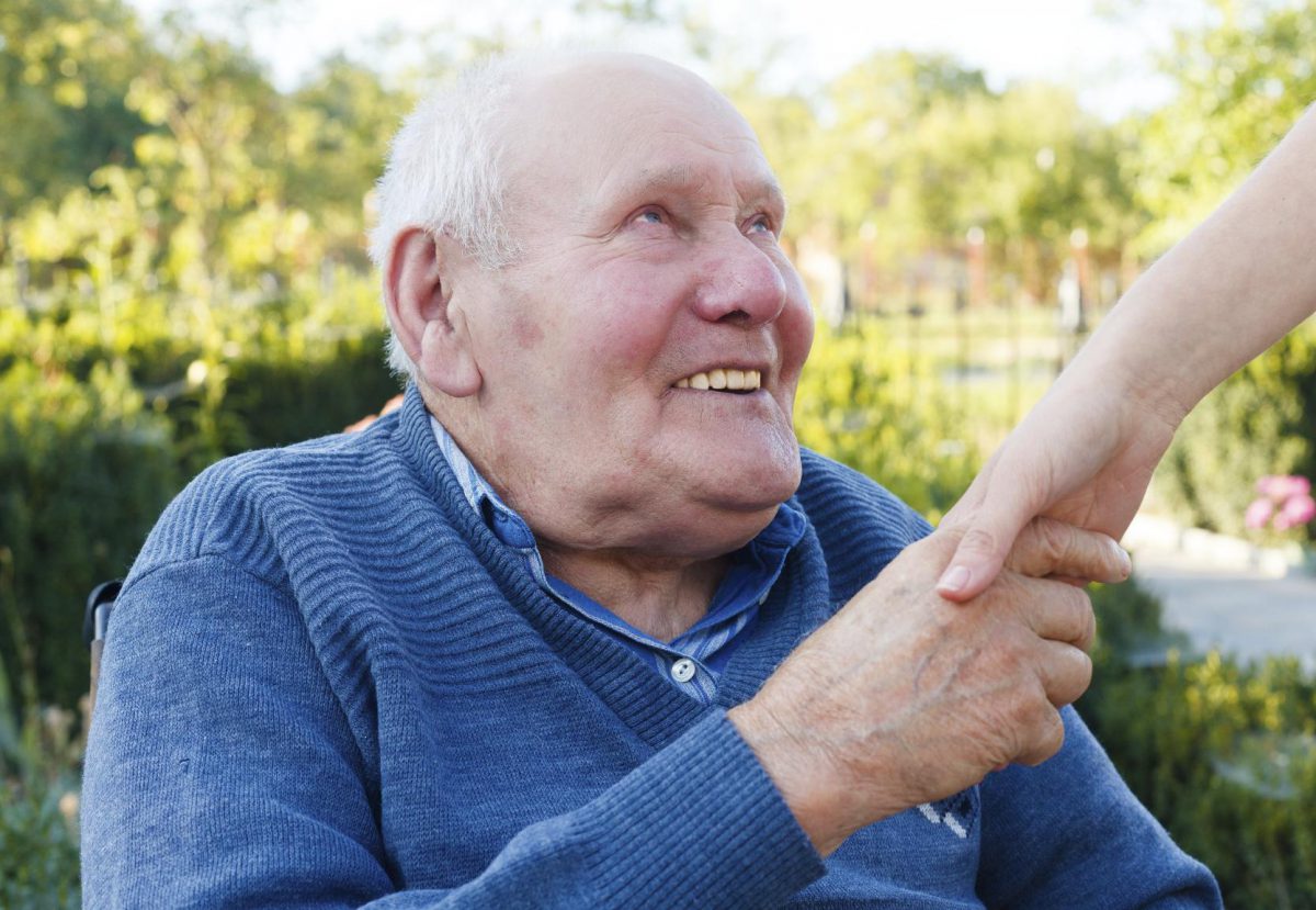 Senior man smiling and grabbing a caregiver's hand.